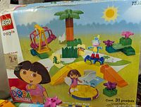 Photo of original box showing front with Dora the Explorer branding and illustration of set components including Dora, Boots, ramp, carousel, palm tree, and flowers.