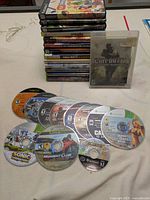 Another angle showing stack of cases and loose discs in front of them, highlighting games for multiple platforms including Xbox, Xbox 360, PS2, Wii, and GameCube.
