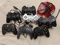 Photo of 8 video game controllers including PlayStation 2 DualShock, Nintendo 64, and Xbox models showing condition and parts.