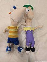 Phineas and Ferb plush toys laid side by side on light surface to show front view, including clothing and details