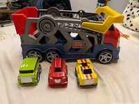 Mega Bloks car carrier truck with three snap-on buildable vehicles in green, red, and yellow positioned in front of the carrier.