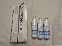 Two Kenmoreclear! replacement water filters in white packaging next to three FilterLogic FL-RF46 filters still sealed in plastic.