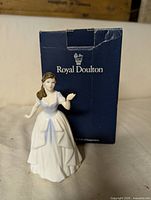 Front view of Royal Doulton figurine next to original blue Royal Doulton box showing size and condition of figurine and packaging.