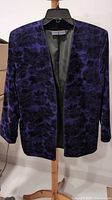 Front view of purple crushed velvet blazer with a subtle darker rose floral pattern. No buttons or collar visible, hung on black hanger.