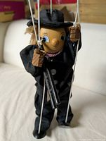 Front view of vintage Tellon marionette chimney sweep with wooden head, hands, black fabric outfit, red checked scarf, black hat and holding wooden chimney ladder.