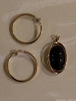 Two 10k gold hoop earrings and a 10k gold pendant with black stone on flat surface.