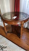 Full view of round wooden accent table with clear glass top showing entire table and three legs visible