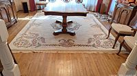 Full view of the wool area rug showing the cream base color with floral pattern and fringed edges.