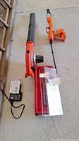 Cordless leaf blower in orange and black with battery charger and battery on concrete floor