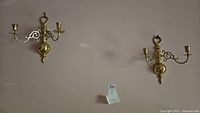 Pair of brass candle sconces mounted on wall, showing overall size and style.