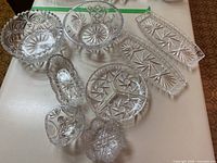 Overview of nine vintage crystal and cut glass dishes and bowls arranged on table showing various sizes and starburst, geometric and crosshatch cut designs.