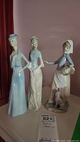 Photo of three porcelain figurines including one NAO by Lladro with a tag showing lot number 521