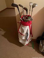 Full view of Wilson golf bag with multiple golf clubs inside, showing white and red colors and club grips.