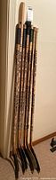 Full set of 7 wooden hockey sticks leaning against wall, taped blades visible