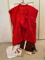 Red silk sleeveless jacket and cap displayed hanging, white tabi socks, geta toggles, bamboo fan, and Bosca leather accessory bag on floor.