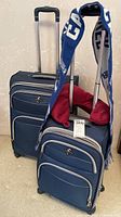 Two navy blue Atlantic rolling suitcases, one with red neck rest and blue Vancouver Canucks scarf draped over the handle.