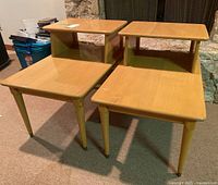 Pair of mid-century modern wooden side tables shown with tiered design, light honey wood finish and tapered legs with brass tips.
