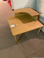 Front view of blonde wood veneer two-tier corner table in basement setting