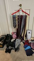 View of assorted neck ties, cummerbunds, scarves, bow ties, and accessory boxes arranged on floor in front of white door with red hanger