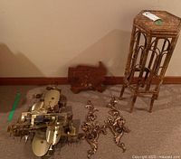 Photo showing the entire lot: two metal candle sconces, wooden clock, metal art piece, and rattan plant stand on carpeted floor against wall.