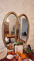 Front view of oval shaped mirror with gold ornate frame placed on table reflecting room.