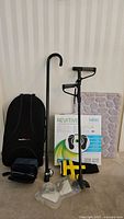 Full lot display showing all items: two canes (traditional and forearm crutch styles), boxed Revitive circulation booster, boxed Medic blood pressure monitor, soft cushioned mat, black Obus Ultra Forme back rest, and plastic accessory pieces.