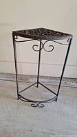 Front-side view of the cast iron triangular plant stand showing scrollwork and leg structure.