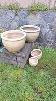 Four ceramic planters placed outside by stone wall, two large and two small sizes.