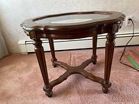 Side view of the wood side table showing carved legs, stretcher base, and glass top insert
