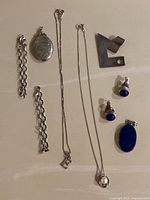 Photo showing all jewelry items laid out including chains, locket, necklaces, earrings, lapis pendant, and silver piece