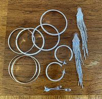 Silver-tone bangles, hoop and tassel earrings arranged on a wooden surface