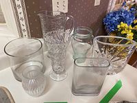 Overview photo of seven assorted clear glass and crystal vases on a table with decorative wallpaper background.