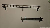 Two wooden wall shelves mounted on a plain wall, showing front spindle railing and mounting brackets.