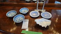 Six porcelain dishes including three Wedgwood jasperware small plates and three Grindley floral bowls, plus one oyster shell shaped dish and two pewter candle holders on wooden table.
