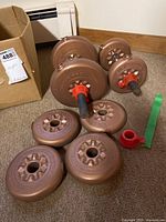 Training weight plates and assembled dumbbells on carpet, cardboard box visible