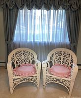 Pair of white wicker chairs front view with pink cushions in room setting