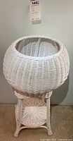 Front view of the white wicker two-tiered round plant stand showing the woven wicker top tier and lower shelf, with sturdy legs.
