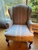 Front view of wingback chair showing upholstery and wooden cabriole legs