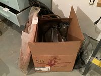 Cardboard box containing a condenser unit with copper tubing protected by piping sleeve and packaging plastic.