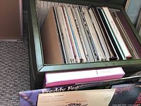 Top view inside storage ottoman showing multiple vintage record albums in sleeves standing upright.