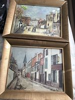 Two framed paintings side by side showing Paris urban street scenes with buildings, a church spire, and people, attributed to Maurice Utrillo.