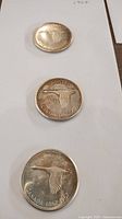 Three 1967 Canadian silver dollar coins laid out vertically on a white surface, showing the flying Canada goose design and inscriptions.
