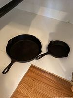 Two black cast iron skillets on a white kitchen counter; one larger and one smaller skillet with handles and spouts.