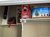 Shelf with boxed moving Santa decoration, boxed 6.5 ft pre-lit Colorado Pine Christmas tree, and other Christmas items.
