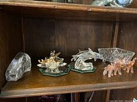 Shelf display of multiple crystal figurines including dolphins, swans, and small art glass elephants with a faceted crystal bowl in background