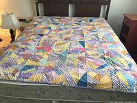 Full view of the double bed-sized patchwork quilt laid out on a bed, showing multiple colorful fabric patches in various patterns.