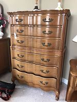 Front angle view of the wooden dresser showing scalloped drawer fronts and attached brass handles.