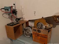 Full lot showing Mastercraft drill press on a wooden shelf, Black & Decker circular saw box, and various hand saws leaning against the wall.