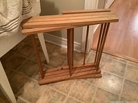 Wooden fold-up drying rack folded up, showing the slatted wooden structure and base with vertical supports.