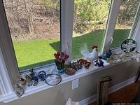 Wide view of windowsill with various animal figurines, floral art, ceramics, and decor items arranged in a row.